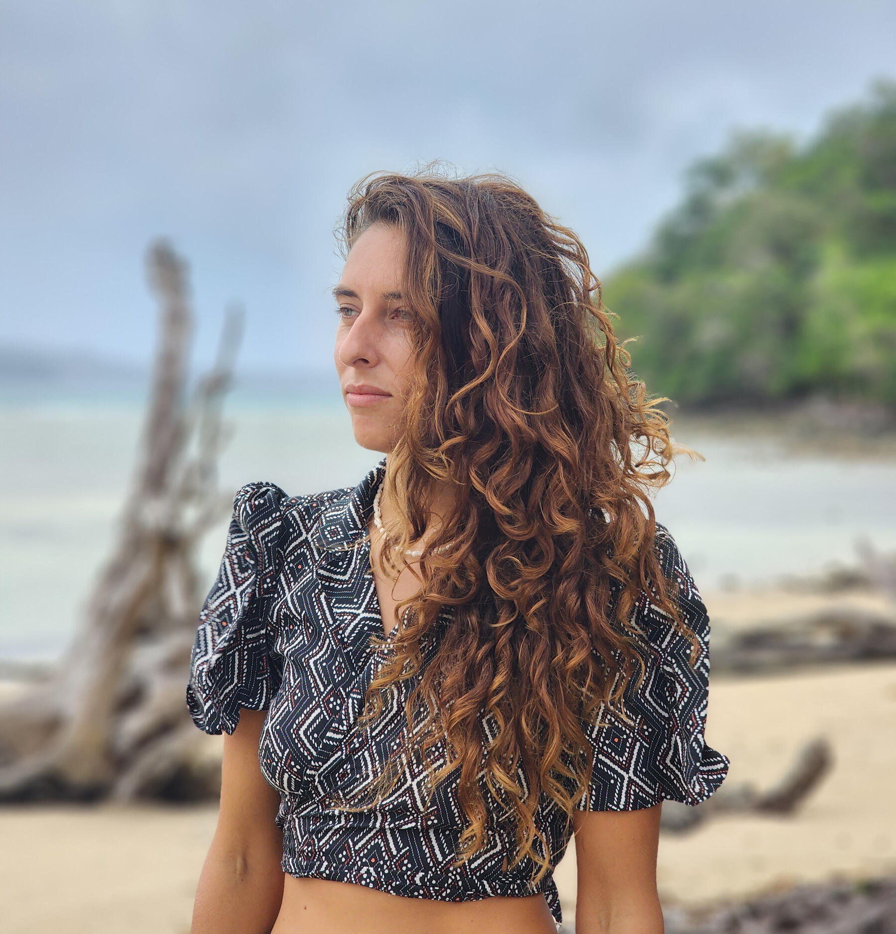 Samara Ruighaver, founder of Inner Shift Wellness Coaching, standing on a quiet beach with curly hair, looking calmly into the distance.